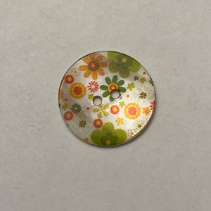 May include: A white button with a floral pattern in shades of orange, yellow, and green. The button has two holes.