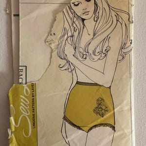 May include: A vintage sewing pattern envelope for lingerie featuring a line drawing of a person wearing high-waisted briefs with lace trim and a floral detail. The yellow and cream paper envelope has torn edges and includes the text Sew Lingerie Pattern by Laver.