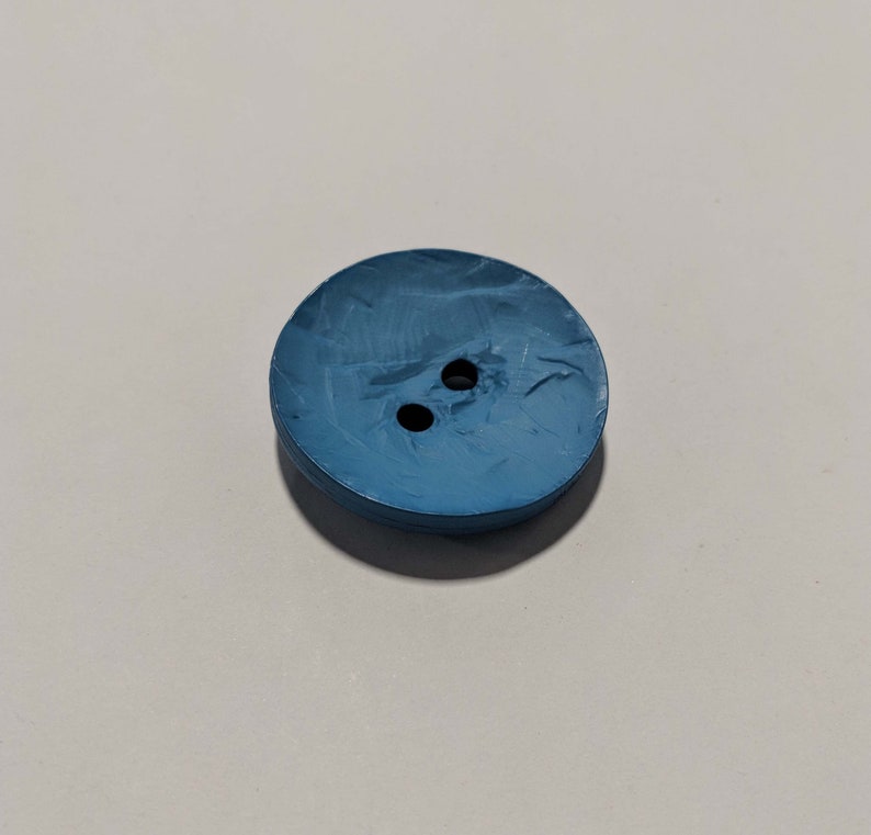 May include: A blue plastic button with two holes. The button has a textured surface.