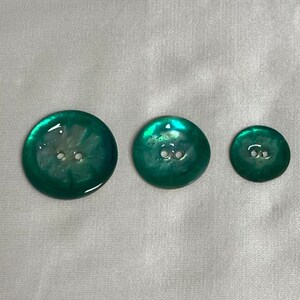 May include: Three iridescent green buttons with two holes each. The buttons are different sizes and have a pearlescent finish.