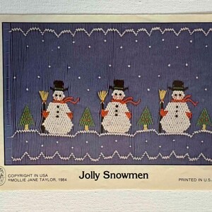 May include: A vintage craft pattern titled "Jolly Snowmen." The design features three snowmen with black top hats, orange scarves, and holding brooms, set against a blue background with falling snow and evergreen trees. The text "PRINTED IN U.S.A." is visible.