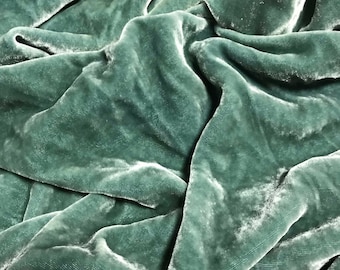 May include: A close-up of a soft, sage green velvet fabric. The fabric is draped and folded, showing its texture and drape.
