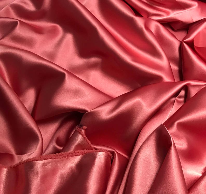 May include: Close-up of a smooth, silky fabric in a deep rose color. The fabric is draped and folded, showcasing its luxurious texture.