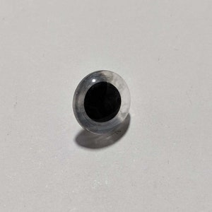 May include: A clear plastic safety eye with a black pupil. The eye is designed for use in crafts and hobby projects.