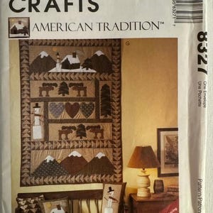 Puede incluir: Un sobre de patrón McCall's Crafts con un diseño de "American Tradition". La imagen muestra un edredón con motivos de montañas, árboles y muñecos de nieve. El patrón también incluye diseños de almohadas con temas invernales similares. El sobre tiene el número 8327.