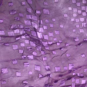 May include: A sheer, purple fabric with a repeating pattern of raised, square shapes. The squares are a slightly darker shade of purple and appear to be satin. The fabric is draped, creating shadows and highlights.