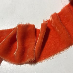 May include: A close-up of a bright orange velvet ribbon with frayed edges. The ribbon is folded and has a soft, luxurious texture.