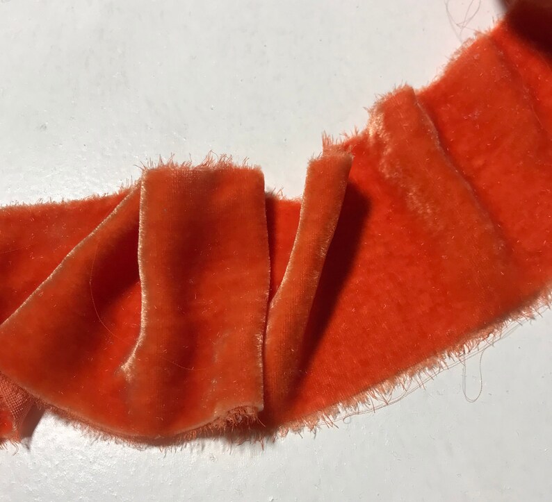 May include: A close-up of a bright orange velvet ribbon with frayed edges. The ribbon is folded and has a soft, luxurious texture.