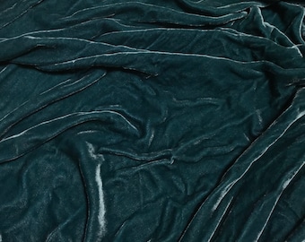 May include: Close-up of a teal velvet fabric with a soft, smooth texture. The fabric is draped and folded, creating a luxurious and elegant look.