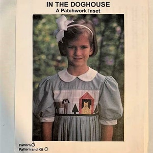 Può includere: Una bambina indossa un vestito azzurro chiaro con un design a patchwork che presenta un cane, un gatto e una casa. Il vestito ha un colletto bianco e maniche a sbuffo. La bambina ha un fiocco bianco nei capelli e sorride. Il testo sull'immagine recita "The Children's Corner IN THE DOGHOUSE A Patchwork Inset Pattern  Pattern and Kit ".