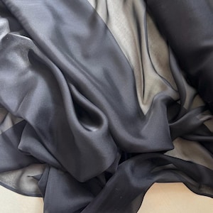 May include: Black sheer fabric with a smooth, silky texture. The fabric is draped and folded, showcasing its transparency and flow.
