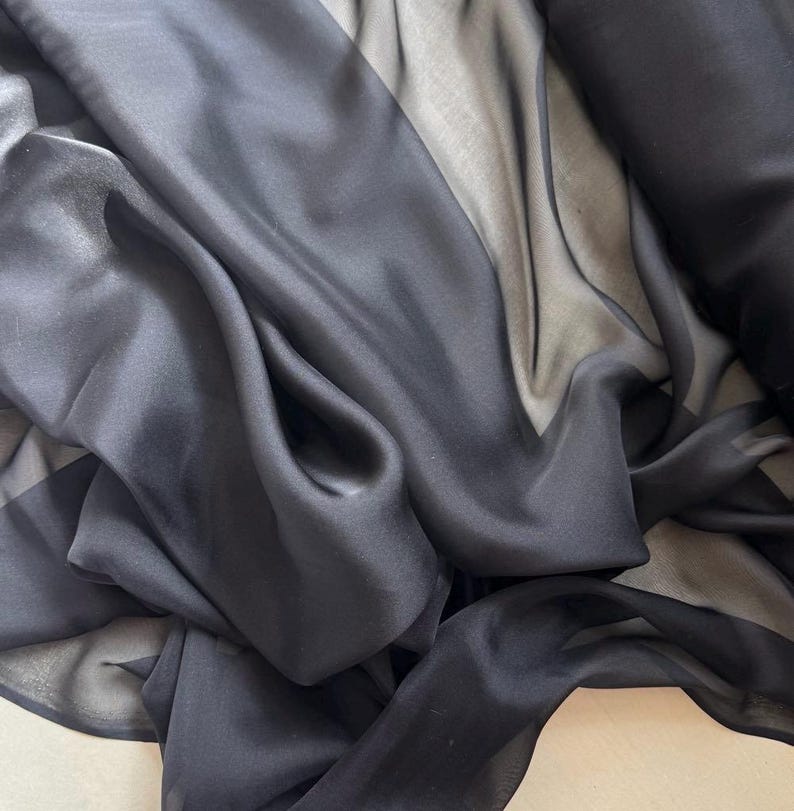 May include: Black sheer fabric with a smooth, silky texture. The fabric is draped and folded, showcasing its transparency and flow.
