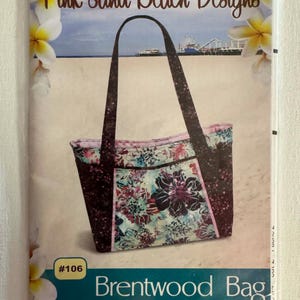 May include: A package for a Brentwood Bag sewing pattern. The bag has shoulder straps, a zipper top, and lots of pockets. The bag's design features a floral pattern with pink and teal accents. The package is labeled "Pink Sand Beach Designs."