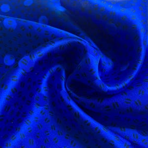 May include: A vibrant royal blue fabric featuring a repeating pattern of small, dark, oval-shaped marks and larger, subtle circular spots. The material has a smooth, reflective surface with deep folds that create a dynamic, flowing appearance.