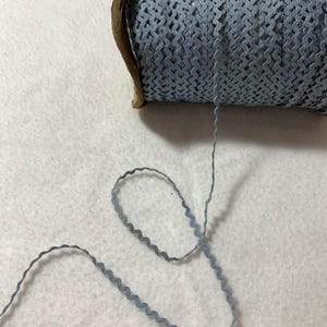 May include: A spool of light blue zig zag trim with a wooden spool. The trim is a wavy, scalloped design.