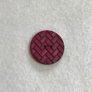 May include: A burgundy button with a woven pattern. The button has two holes.
