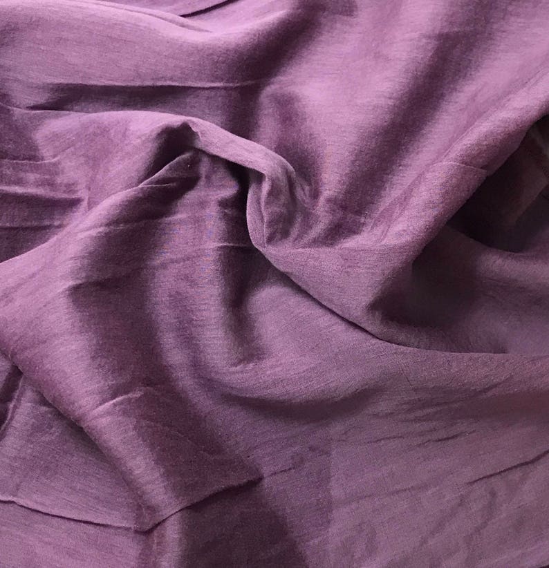 May include: A close-up of a smooth, soft, purple fabric with a subtle sheen. The fabric is draped and folded, creating a textured surface.