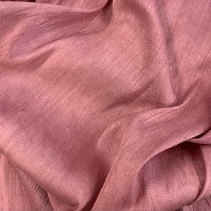 May include: Close-up of a soft, pink fabric with a subtle sheen. The fabric has a smooth, silky texture and a slightly wrinkled appearance.