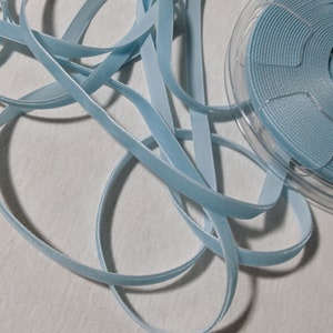 May include: A spool of light blue velvet ribbon. The ribbon is wound around a clear plastic spool.