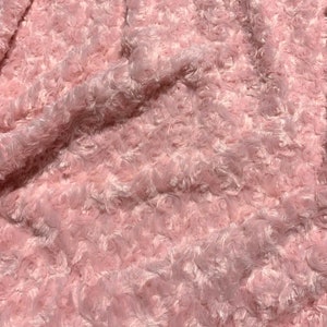 May include: A close-up shot of a soft, pink fabric with a rose-like texture. The material is plush and fluffy, with a dense pattern of small, swirling shapes. The overall effect is delicate and inviting, suggesting a cozy blanket or decorative textile.
