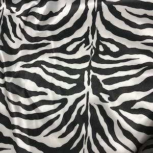 Könnte beinhalten: Schwarz-weißes Zebra-Mustergewebe mit Satin-Finish. Der Stoff hat eine glatte, seidige Textur.
