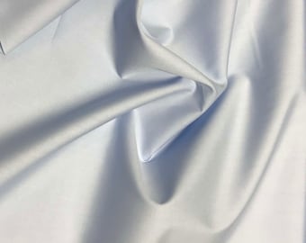 Può includere: Un tessuto liscio di colore azzurro chiaro con una texture setosa. Il tessuto è piegato e drappeggiato, mostrando la sua natura morbida e fluida.