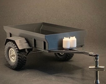 Peut inclure: Une remorque utilitaire noire avec de gros pneus tout-terrain et deux petits réservoirs de propane blancs. La remorque a une caisse rectangulaire et un attelage argenté. Les pneus ont un motif de bande de roulement détaillé.