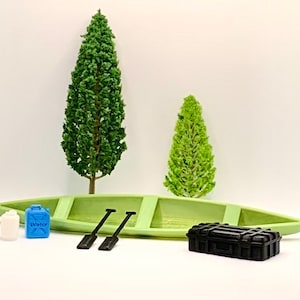Könnte beinhalten: Eine Miniatur-Diorama-Szene mit einem hellgrünen Kanu, zwei grünen Bäumen, zwei schwarzen Paddeln, einem schwarzen Koffer, einer weißen Flasche und einem blauen Wasserbehälter mit dem Wort "WATER". Die Szene spielt vor einem weißen Hintergrund.