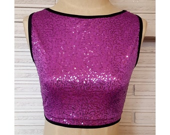Può includere: Un top corto senza maniche con paillettes e bordino nero. Il top è realizzato in tessuto viola con paillettes.