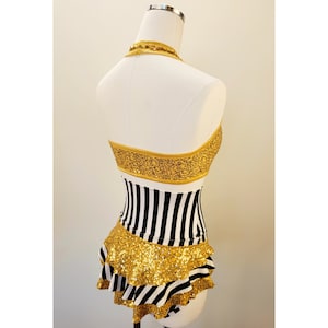 May include: A black and white striped skirt with a gold sequined ruffle trim. The skirt is on a white mannequin.