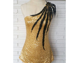 May include: A gold sequined one-shoulder dress with a black feather design on the shoulder.
