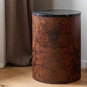 May include: A cylindrical wooden cabinet with a black marble top. The cabinet has a rich, dark brown wood grain pattern. The doors have small gold-colored handles. The cabinet is approximately 76 cm tall.