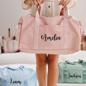 May include: Three personalized duffel bags in pink, blue, and green with the names Amelia, Liam, and Jackson printed on them.