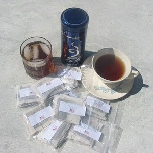 Peut inclure: Une bo&icirc;te &agrave; th&eacute; bleue avec un motif blanc, une tasse de th&eacute;, un verre de th&eacute; glac&eacute; et un tas de sachets de th&eacute;. Les sachets de th&eacute; sont emball&eacute;s individuellement dans du plastique transparent et portent une &eacute;tiquette blanche avec du texte noir.