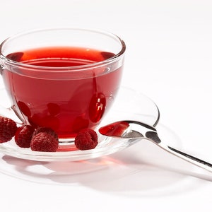 Peut inclure: Une tasse &agrave; th&eacute; en verre transparent remplie de th&eacute; rouge &agrave; la framboise, pos&eacute;e sur une soucoupe avec quatre framboises fra&icirc;ches. Une cuill&egrave;re &agrave; caf&eacute; en argent repose sur la soucoupe.