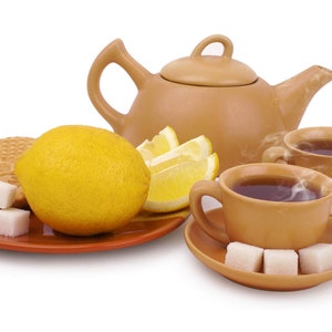Puede incluir: Una tetera marr&oacute;n con una taza de t&eacute; marr&oacute;n y un platillo, un lim&oacute;n, rodajas de lim&oacute;n y terrones de az&uacute;car en un plato marr&oacute;n.