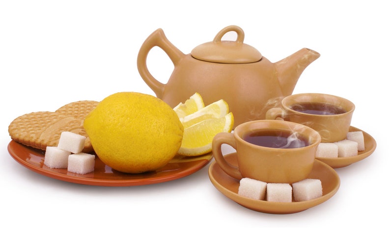 Puede incluir: Una tetera marr&oacute;n con una taza de t&eacute; marr&oacute;n y un platillo, un lim&oacute;n, rodajas de lim&oacute;n y terrones de az&uacute;car en un plato marr&oacute;n.