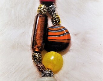 Puede incluir: Un llavero con un anillo de plata y un cordón de cuero. La cadena está decorada con cuentas de vidrio de colores en tonos rojos, naranjas, amarillos y marrones.