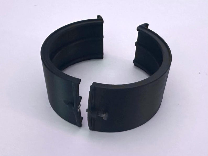 K&ouml;nnte beinhalten: Ein schwarzes, halbkreisf&ouml;rmiges Objekt, das in zwei Teile geteilt ist, mit einer Nut entlang des inneren Umfangs. Das Objekt scheint aus einem gummiartigen Material zu bestehen. Die Teile sind leicht getrennt und zeigen einen kleinen Verbinder.