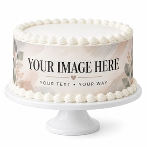 May include: A round cake on a white pedestal stand featuring a white frosting border. The side of the cake displays a watercolor botanical design with the text "YOUR IMAGE HERE" above a small heart and the text "YOUR TEXT • YOUR WAY".
