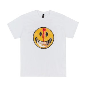 以下が含まれることがあります： 弾痕のある、黄色のスマイリーフェイスのグラフィックが施された白いTシャツ。 グラフィックは、赤い血のディテールを持つ頭蓋骨のような外観をしています。 シャツは、クラシックなクルーネックです。