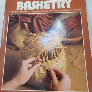May include: A book titled "Basketry: A complete introduction to coiled and woven basketry. Illustrated in full colour." by Rachel Seidel Gilman and Nancy Bess. The cover features a close-up of a person's hands weaving a basket.