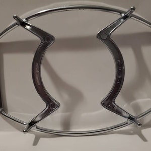 May include: A silver metal rack with two handles. The rack is designed to hold a round object, such as a cake or a pie. The rack has a label that reads "GOODRICH STAINLESS".