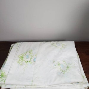 Puede incluir: Un conjunto de sábanas blancas con un patrón floral que presenta hojas verdes y flores azules y blancas.