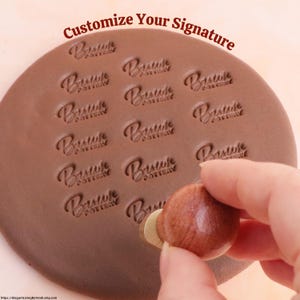 May include: A brown pottery stamp with the text "Bristol Pottery" repeatedly stamped on a brown clay surface. The stamp is being used with a wooden handle. The text "Customize Your Signature" is at the top.