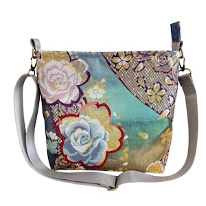 以下が含まれることがあります： グレーの調節可能なストラップが付いた、花柄のショルダーバッグ。 バッグは、ピンク、青、金色の大きな刺繍の花のデザインが、ターコイズと紫色の背景に施されています。