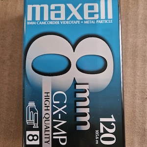 May include: A Maxell 8mm camcorder videotape box. The box is blue with white text and graphics, including the number "8" in a large, stylized font. The box also indicates "120" and "105.6 m".