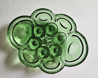 May include: A green glass serving dish with a distinctive, cloud-like form. It has a central starburst design, encircled by circular and oval indentations of varying sizes. The rim is decorated with a scalloped edge.