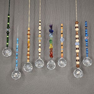 Könnte beinhalten: Eine Sammlung von Kristall-Sonnenfängern mit verschiedenen Perlen- und Steinakzenten. Jeder Sonnenfänger hat eine klare Kristallkugel, die an einer Schnur hängt, mit bunten Perlen und Edelsteinen in Grün-, Blau-, Braun- und Regenbogenfarben.
