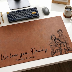 May include: A brown leather desk mat with the text "We love you, Daddy" and the names "Sophia & Lucas". The mat features a sketch of a family. A keyboard, mouse, and monitor are visible in the background.
